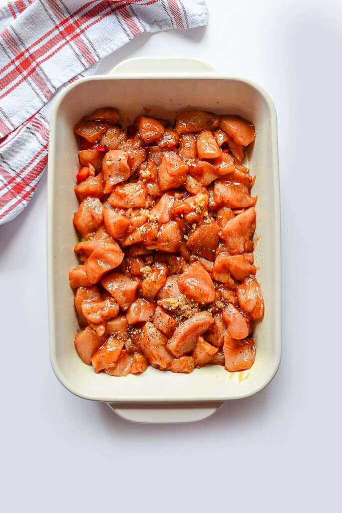 Chicken being added to a white baking dish.