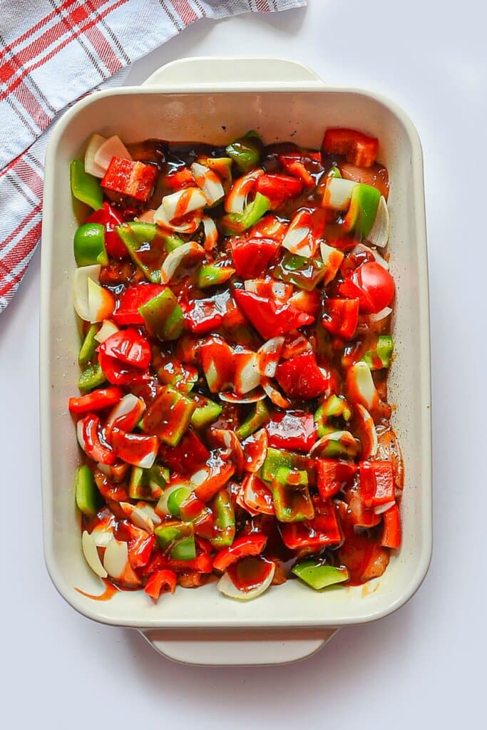 Sauce being poured on top of chopped vegetables in a white baking dish.