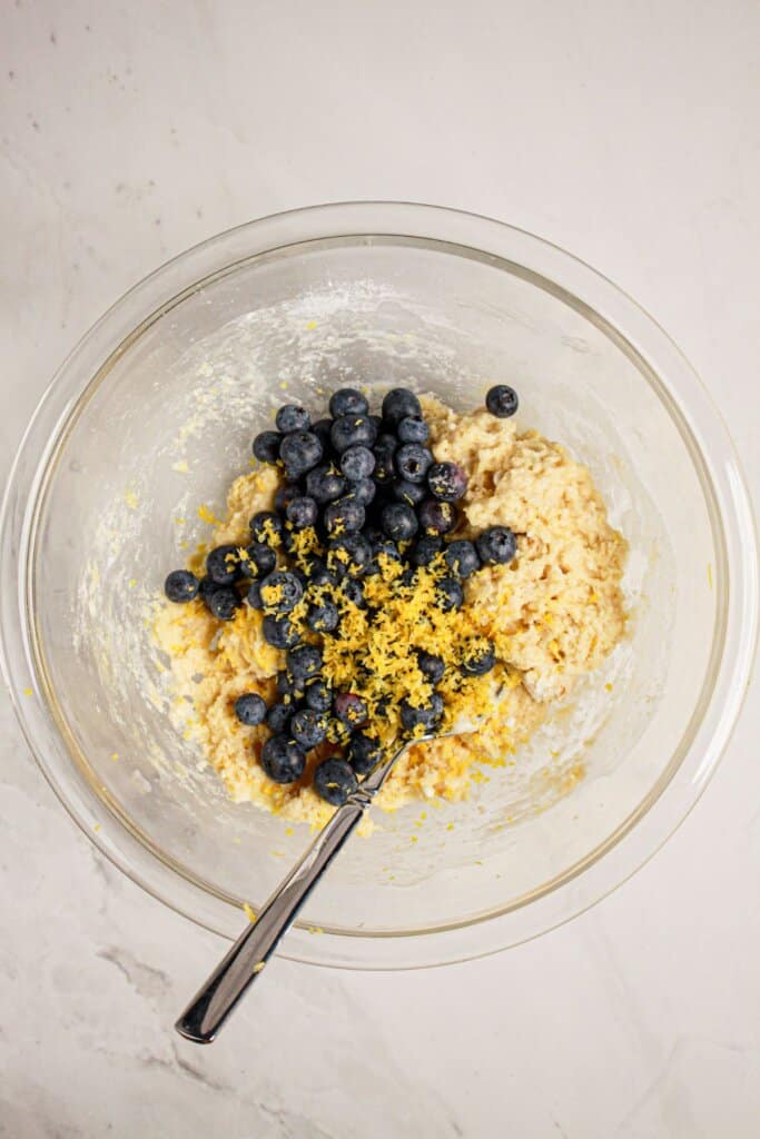 Fruit and zest being added to dough in a glass bowl.