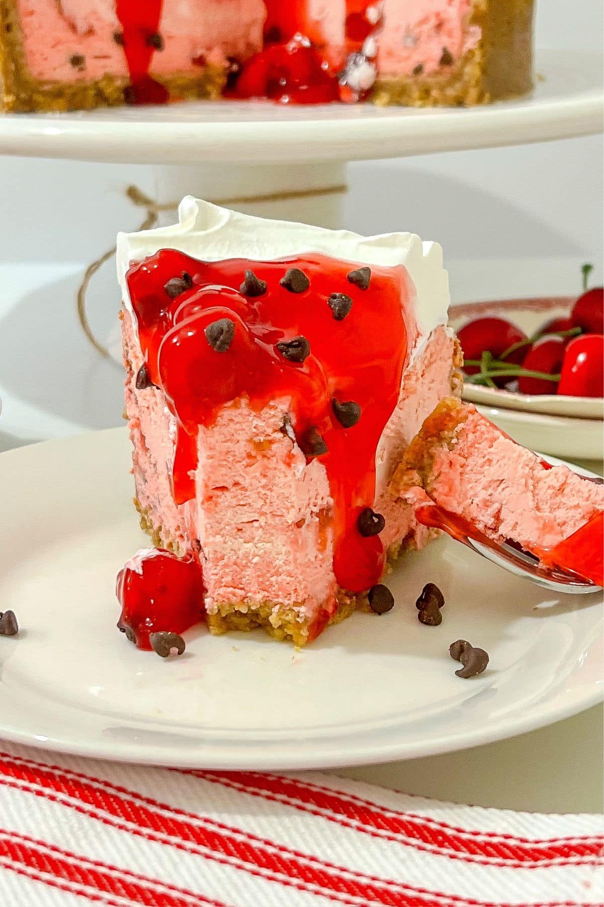 Slice of cherry chip cheesecake on a white plate.