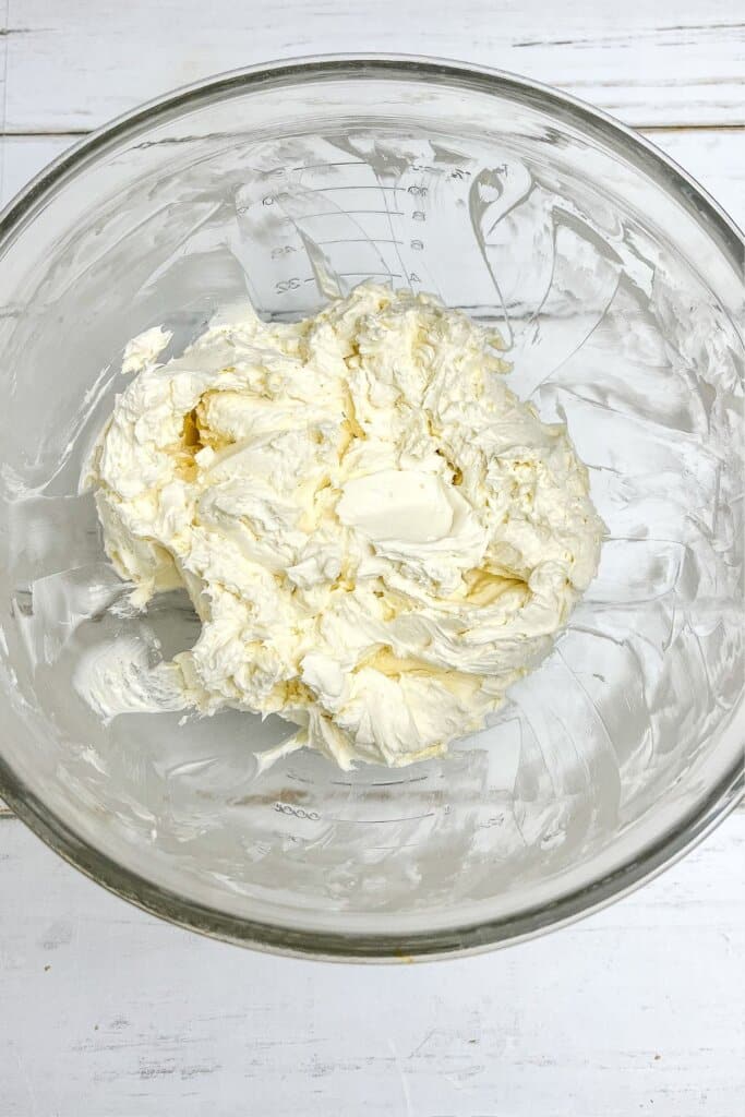 Cream cheese being mixed in a glass bowl.