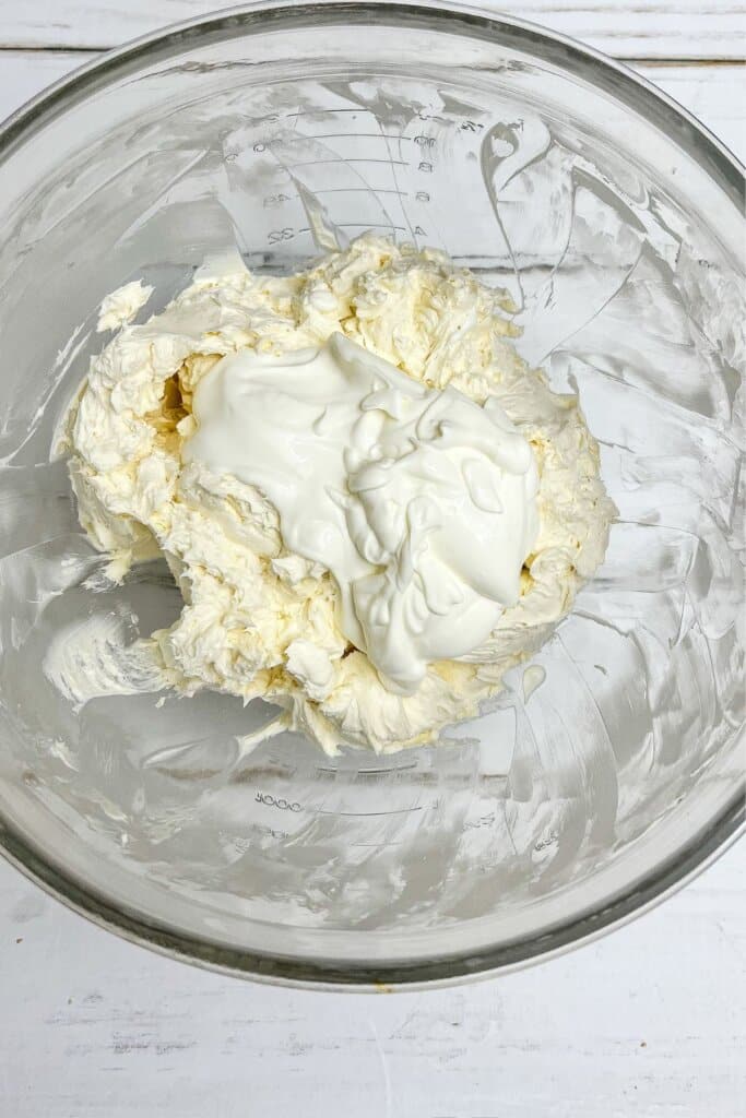 Sour cream being added to batter in a glass bowl.