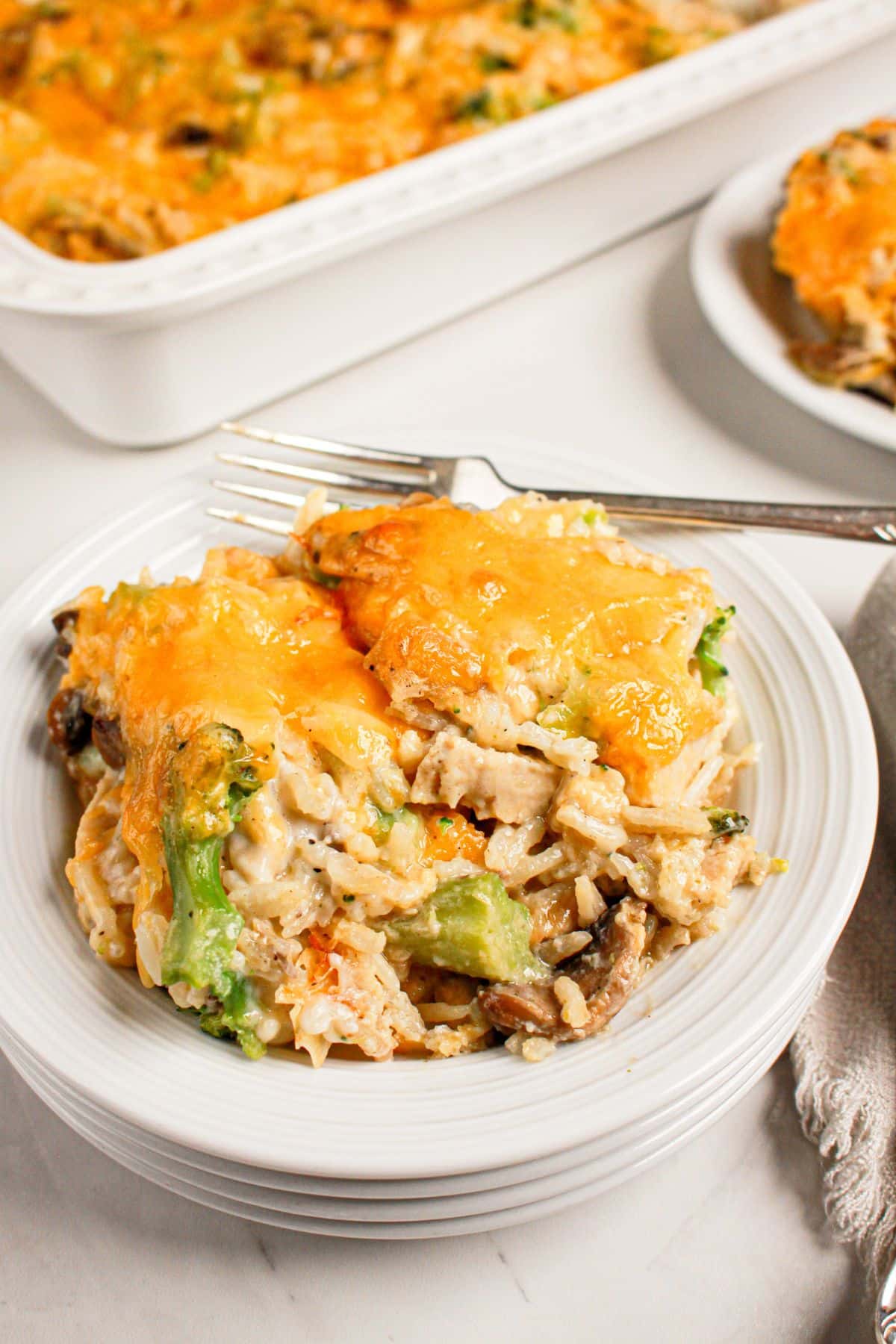Serving of chicken broccoli and rice casserole on a stack of white plates.