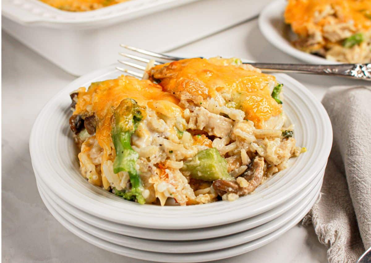 Serving of chicken broccoli and rice casserole on a stack of white plates.