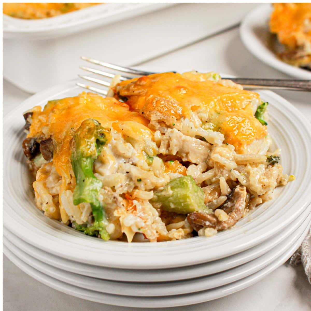 Serving of chicken broccoli and rice casserole on a stack of white plates.