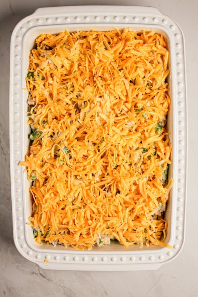 Cheese being sprinkled on top of vegetables in a baking dish.