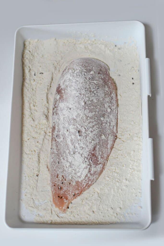 Chicken breasts being breaded in a white plate.