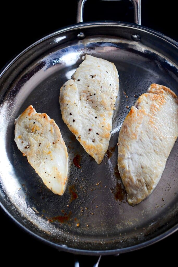 Chicken breasts being seared in a skillet.