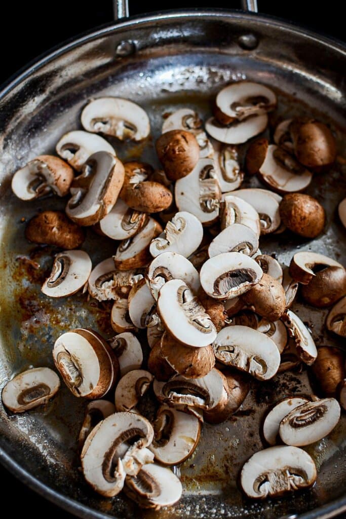 Mushrooms being cooked in a large skillet.