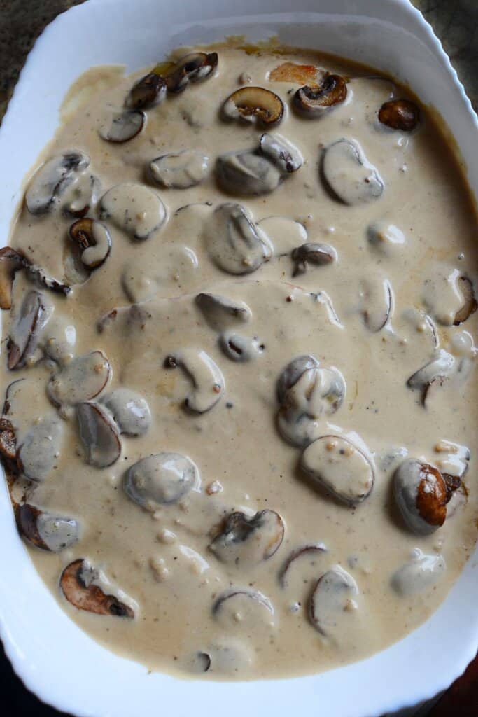 Mushroom cream sauce on top of food in a white baking dish.