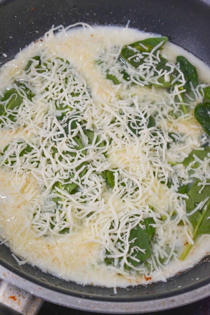 Cheese on top of spinach in a skillet.