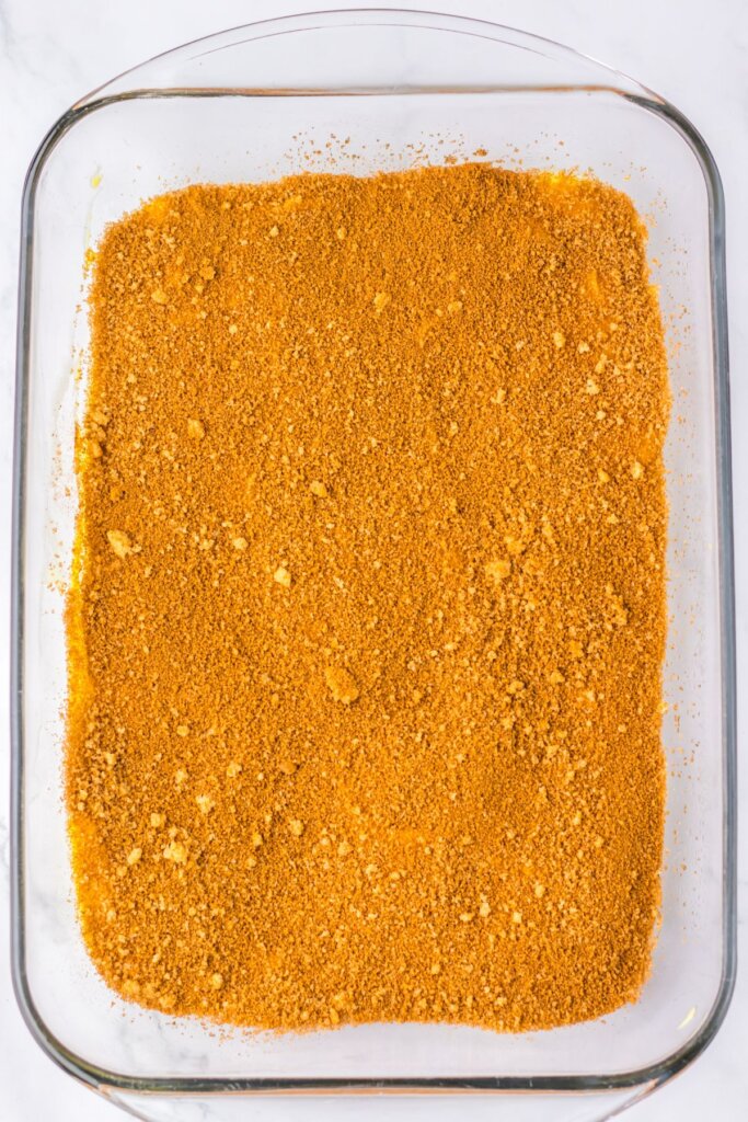 Cinnamon sugar mixing being sprinkled on top of batter in a glass baking dish.