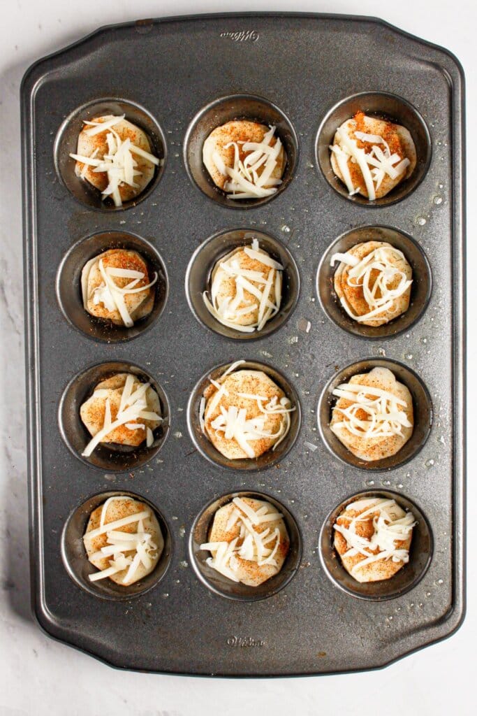 Cheese being sprinkled into muffin tin.