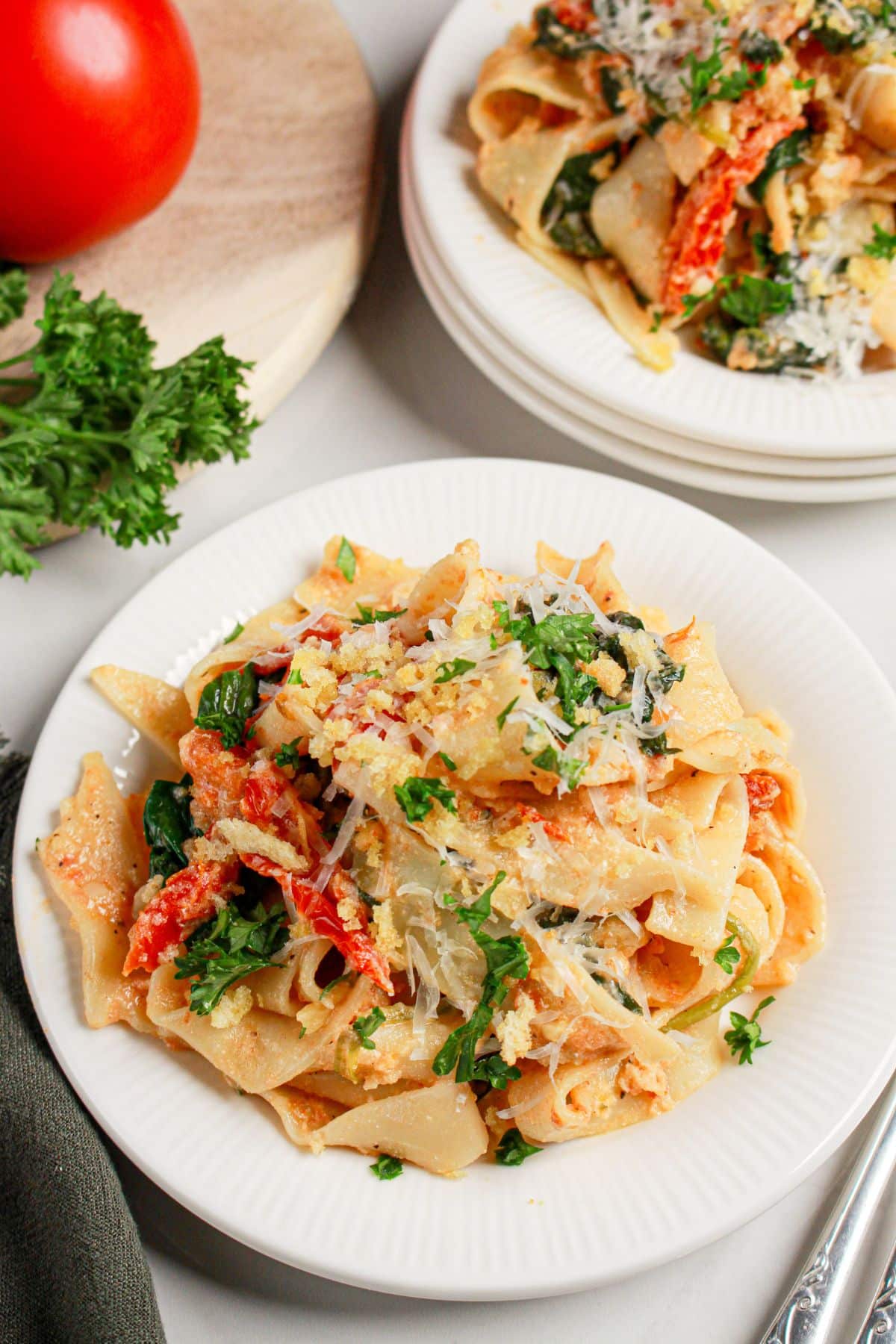 White plate full of pasta with spinach and tomatoes.