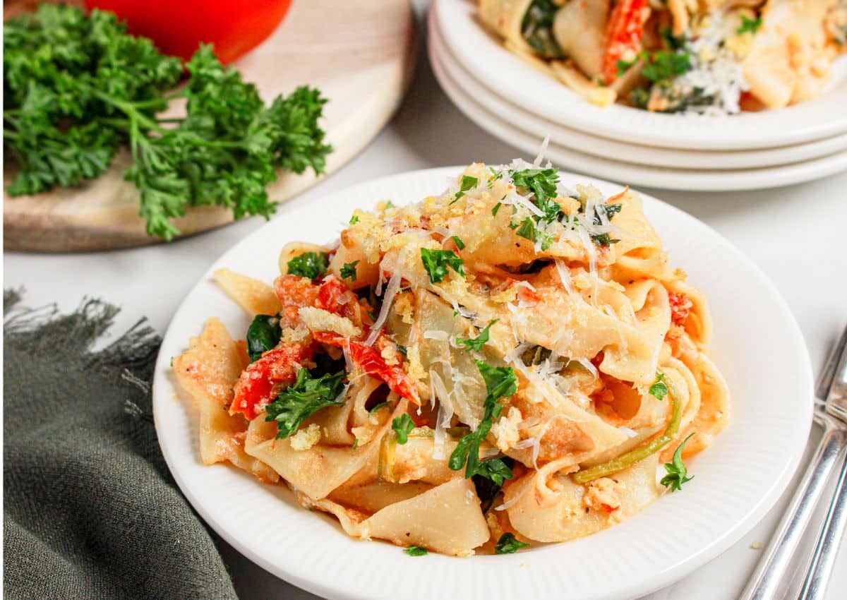 White plate full of pasta with spinach and tomatoes.