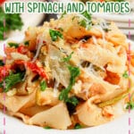 White plate full of pasta with spinach and tomatoes.