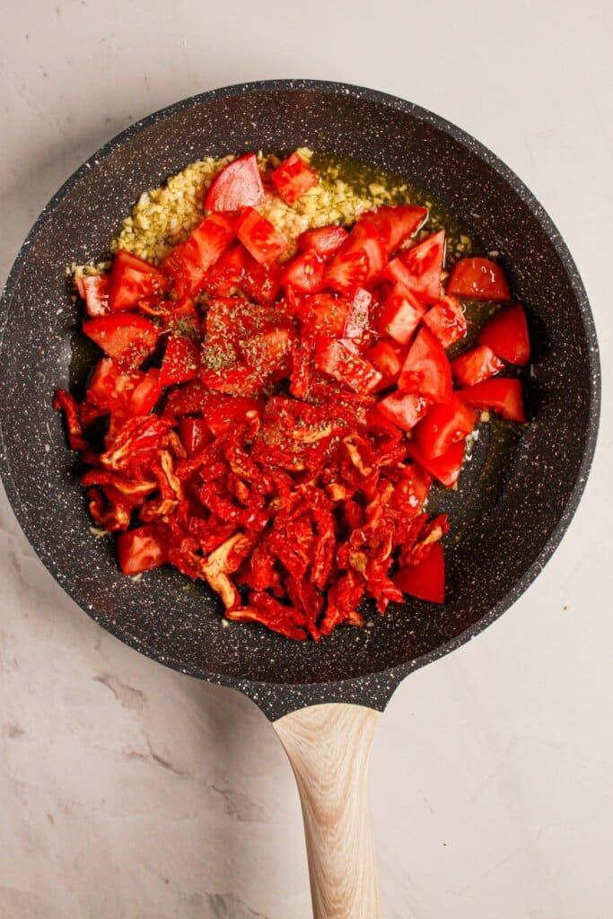 Tomatoes and garlic being sauteed in a skillet.