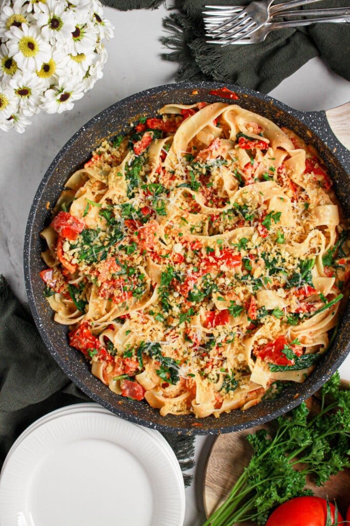 Skillet full of pasta with spinach and tomatoes.