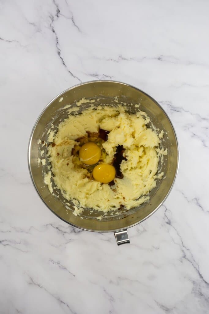 Eggs and vanilla being added to dough in a mixing bowl.