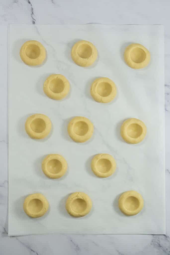 Dough with thumbprints pressed inside on parchment paper.