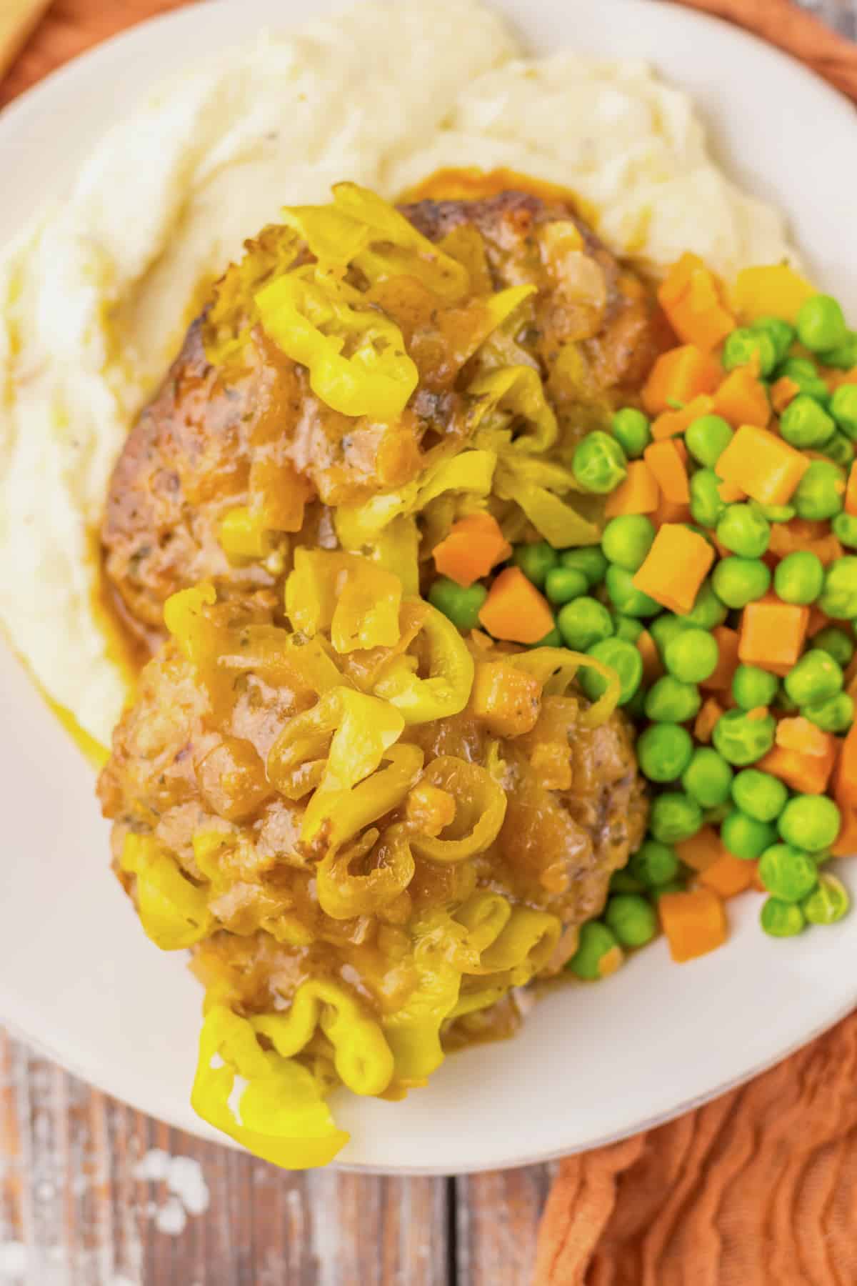 Salisbury steak on a plate with peas and carrots.
