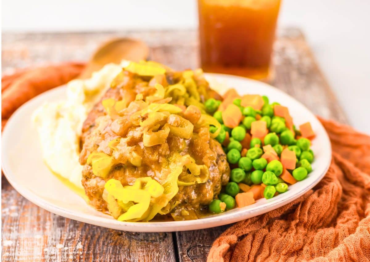 Salisbury steak on a plate with peas and carrots.