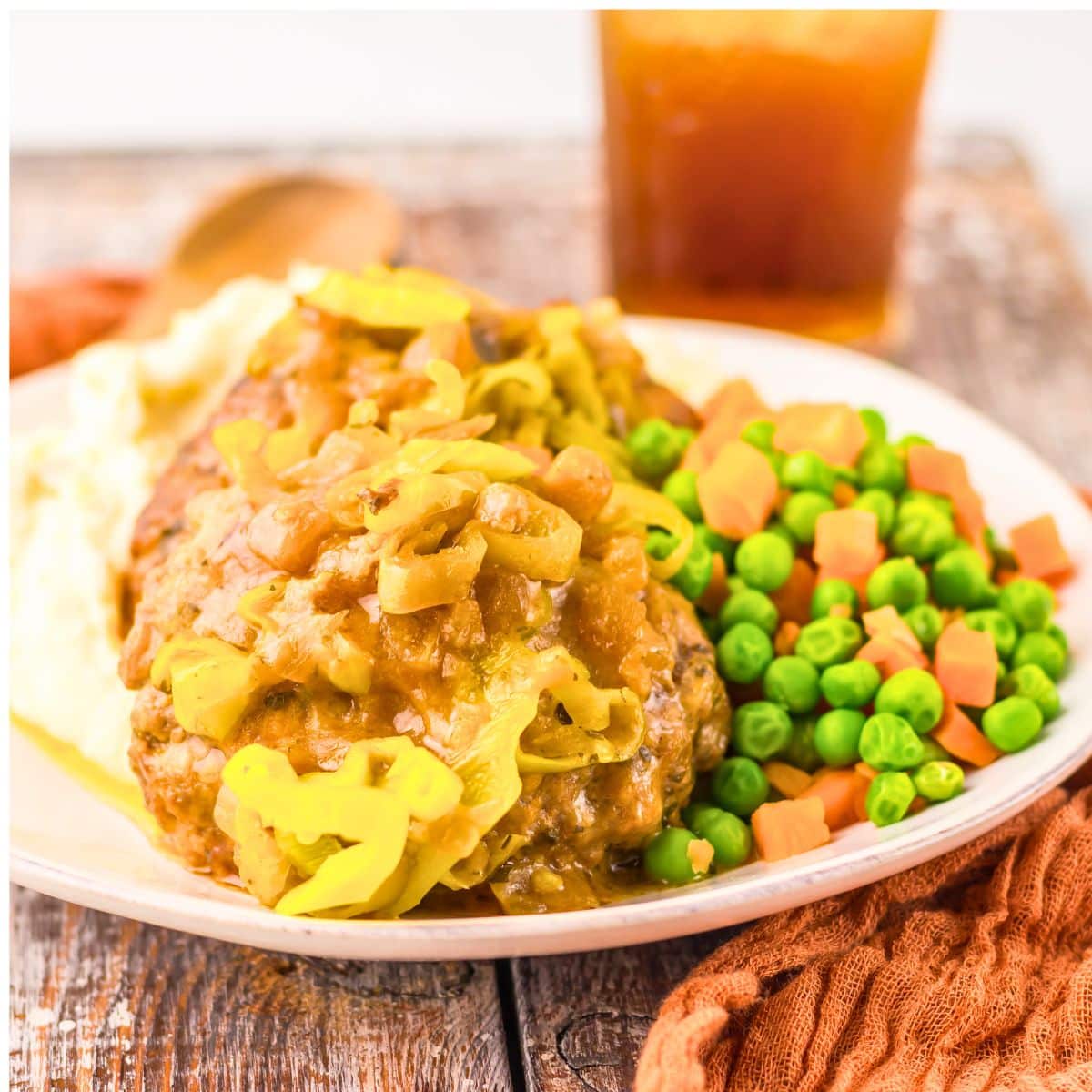 Salisbury steak on a plate with peas and carrots.