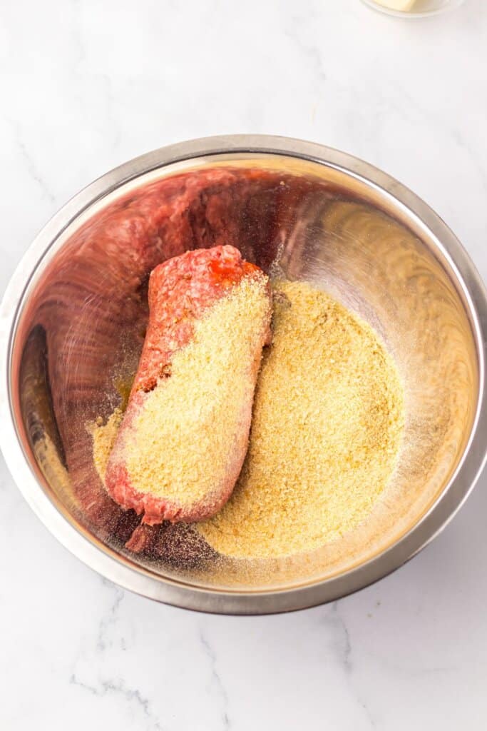 Meat and bread crumbs being mixed in a stainless steel mixing bowl.