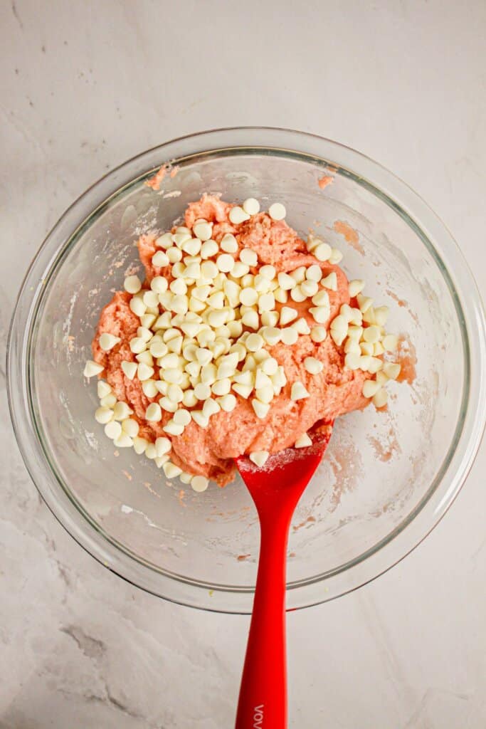 White chocolate chips being folded into batter in a glass bowl.