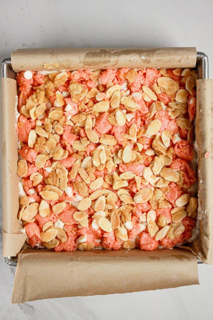 Almonds being added to the top of a dessert in a baking dish.