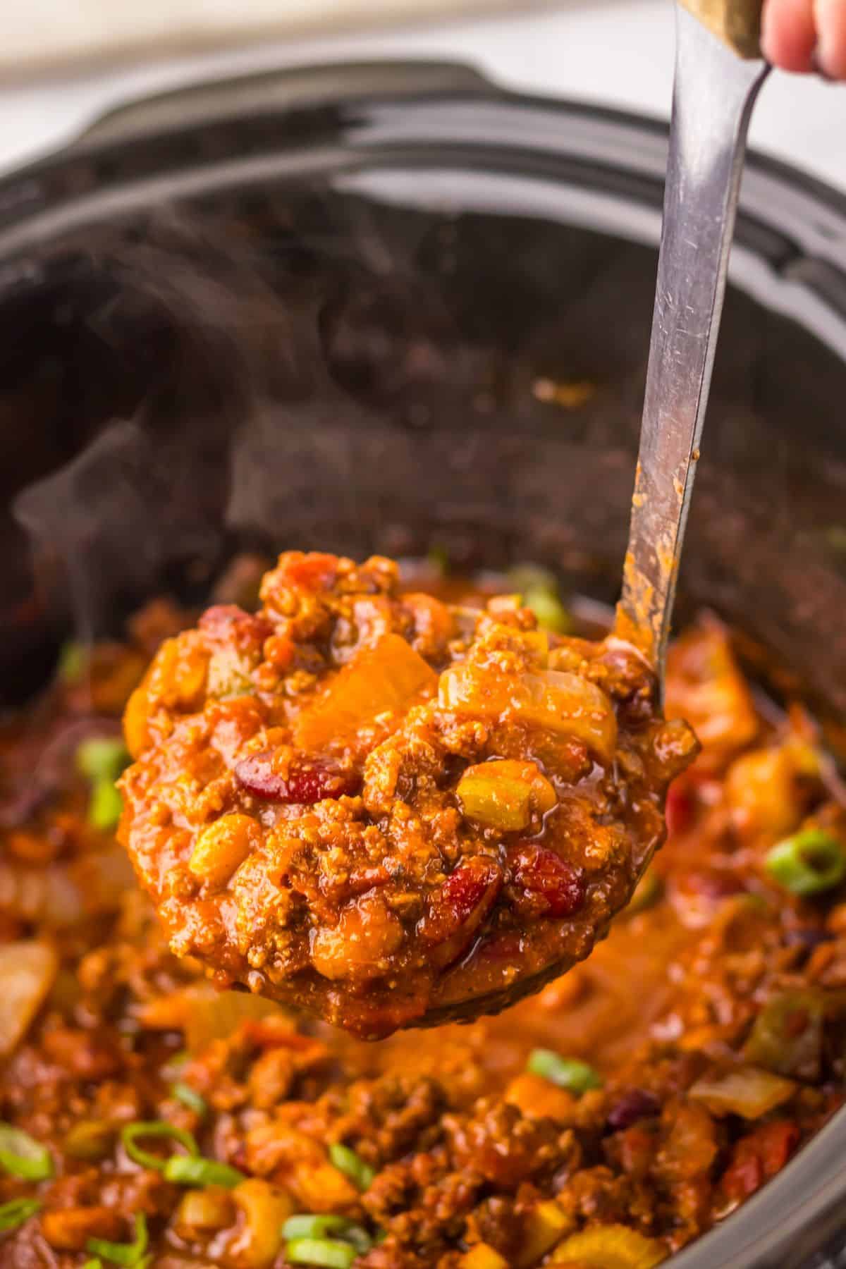 Ladle full of chili being removed from a crock pot.