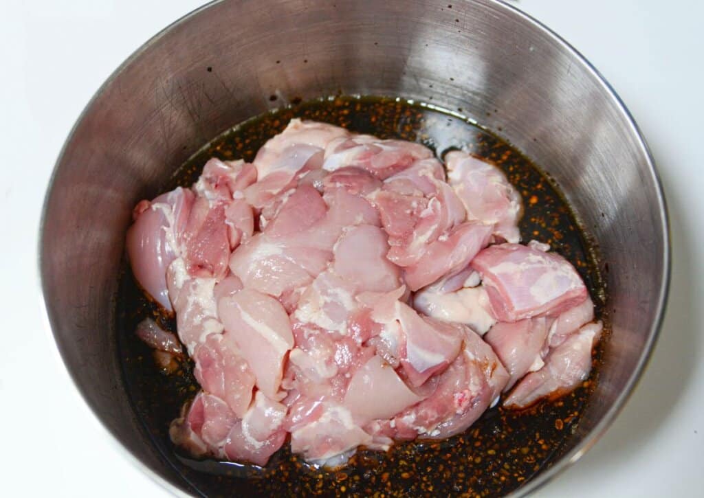 Chicken being marinated in a stainless steel bowl.