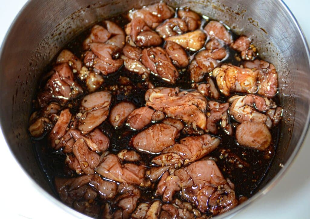 The meat is being soaked in the marinade in a mixing bowl.