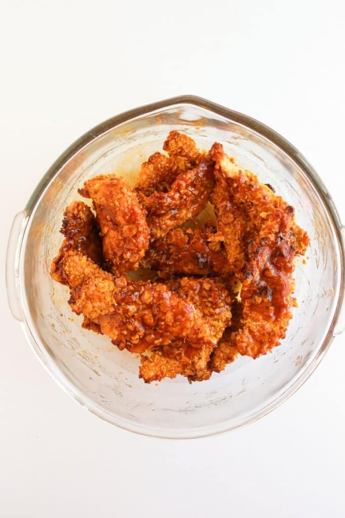 Meat being tossed in a sauce in a glass bowl.