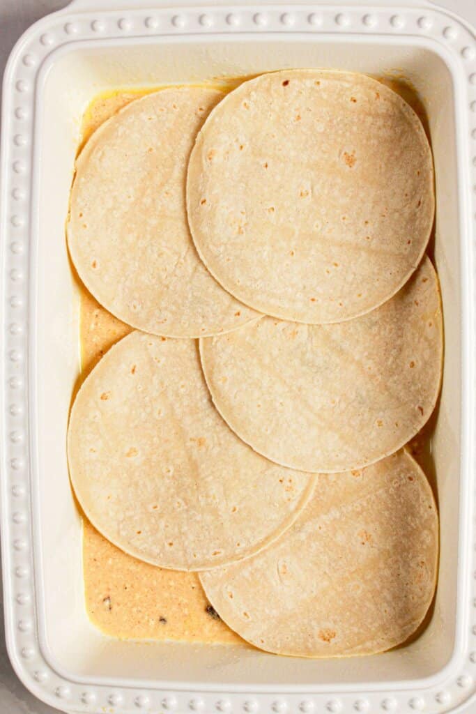 Tortillas being layered in baking dish.