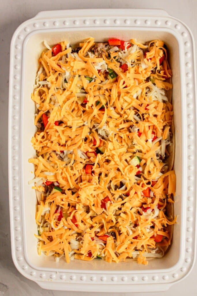 Cheese being sprinkled on top of baking dish.