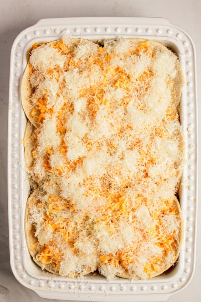 Cheese being sprinkled on top of food in a baking dish.