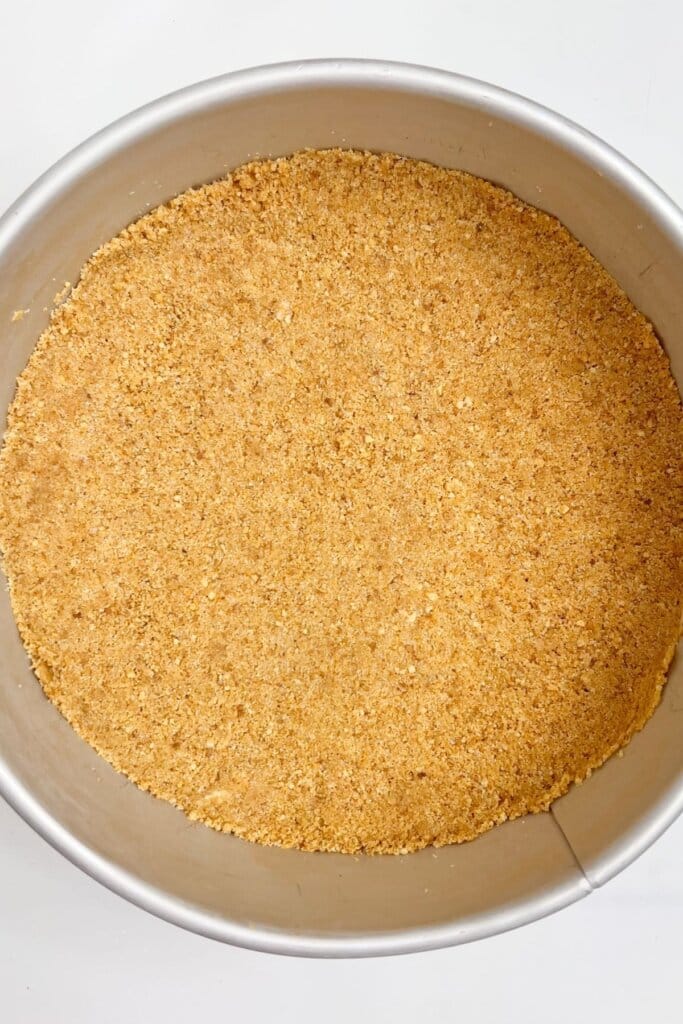 Graham cracker crust being pressed into a springform pan.