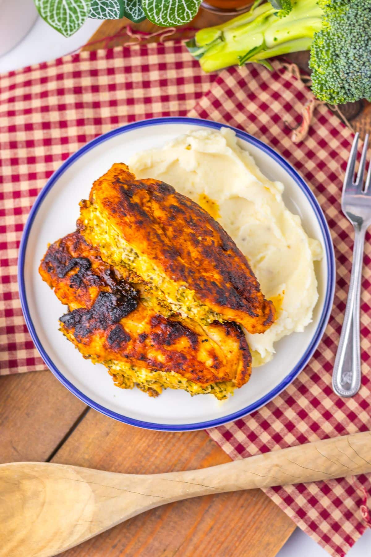 Broccoli stuffed chicken breasts on a plate with mashed potatoes.