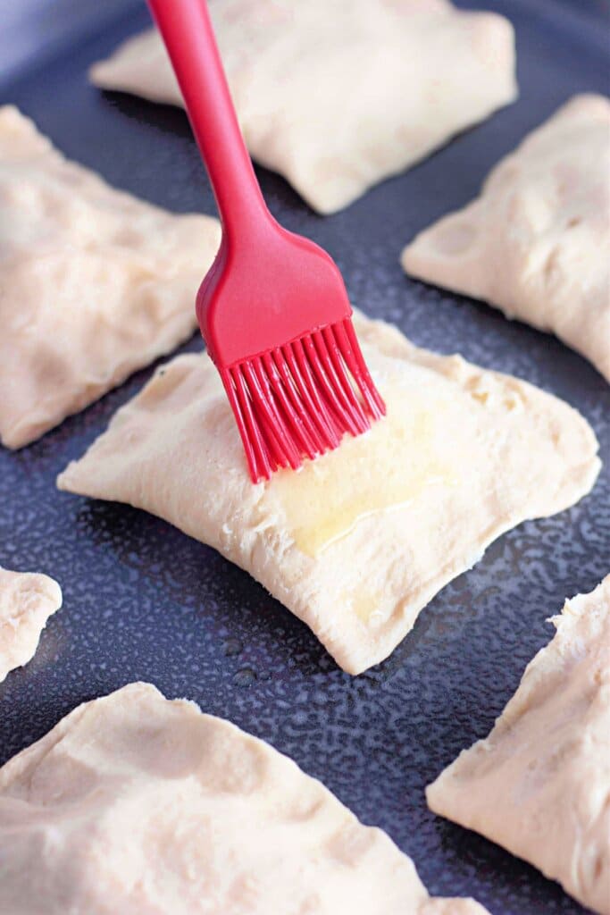 Butter being brushed on top of pastries on a baking dish.