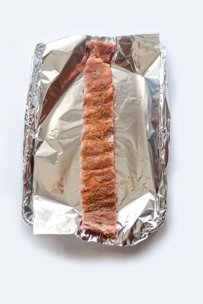 Meat being seasoning on a baking sheet.