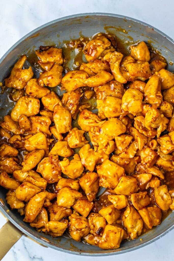 Meat being tossed in sauce in a skillet.