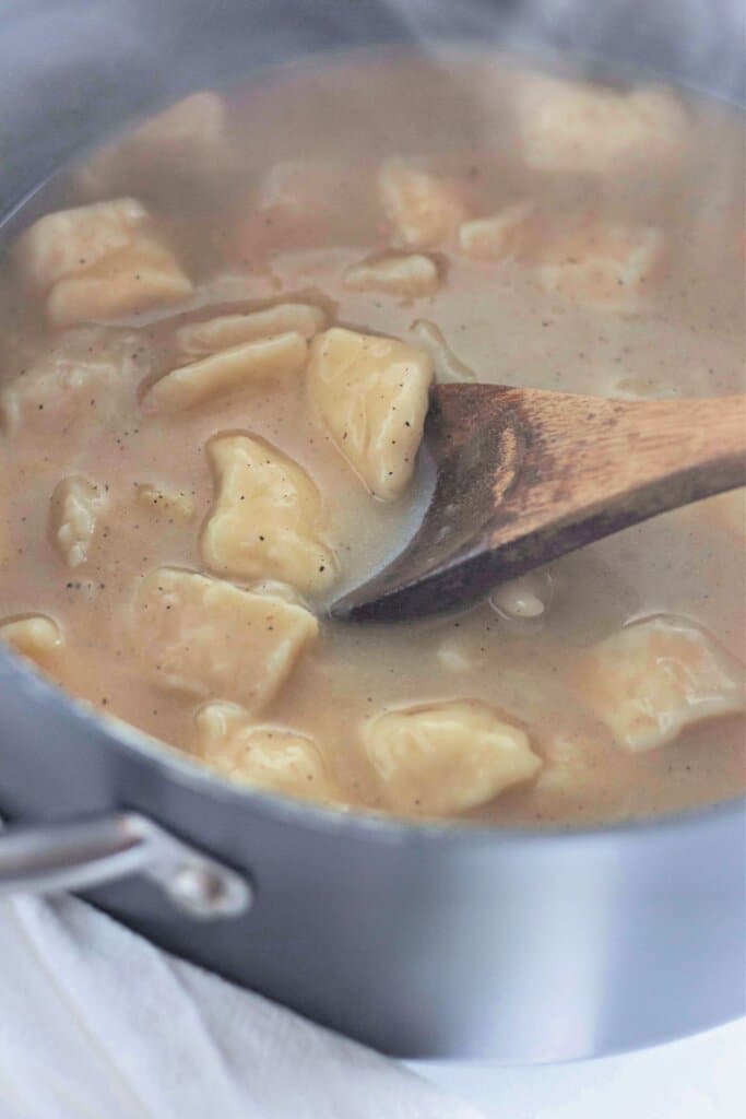 Soup being stirred with a wooden spoon in a pot.