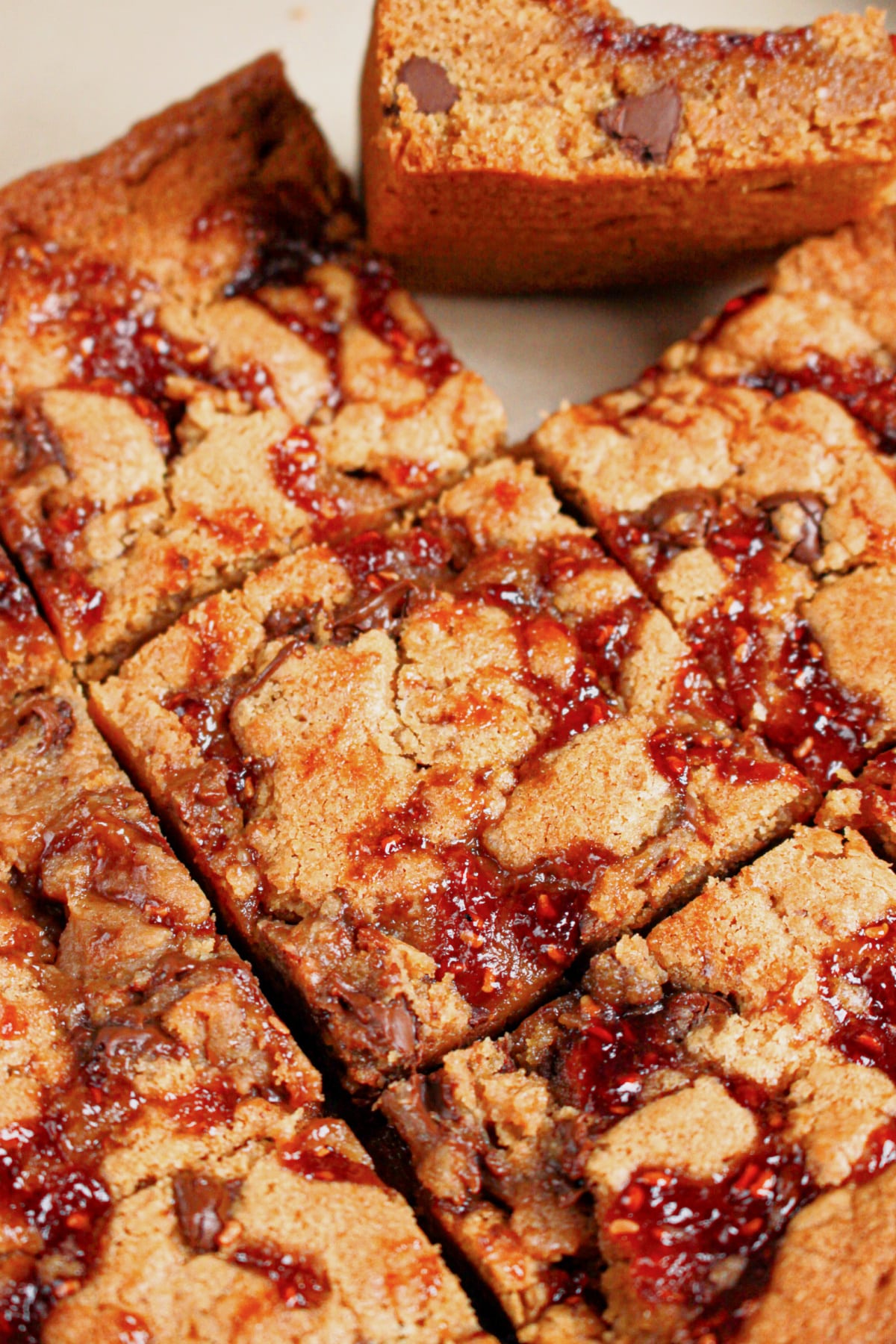 Peanut butter chocolate chip brownies topped with jam cut into squares.