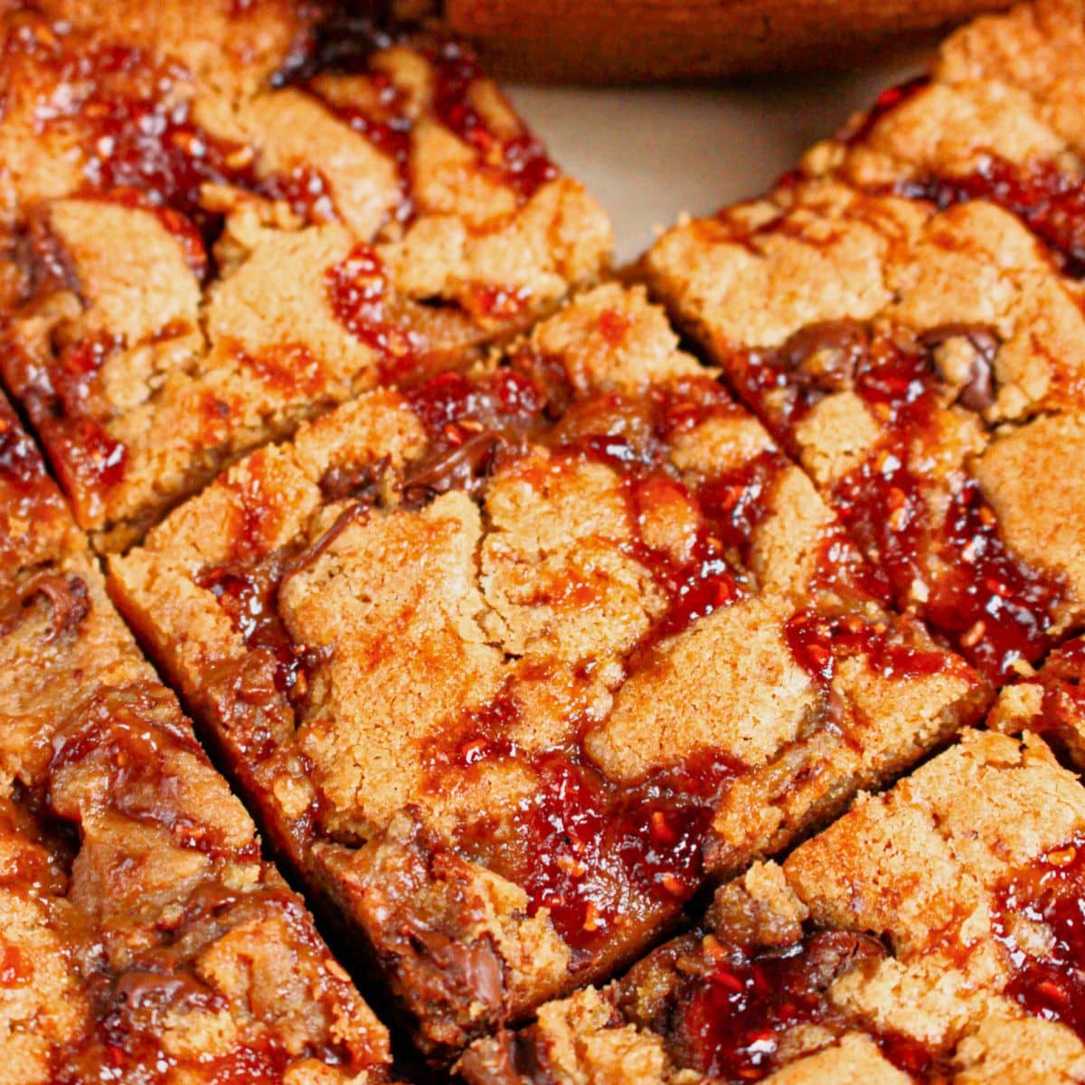 Peanut butter chocolate chip brownies topped with jam cut into squares.