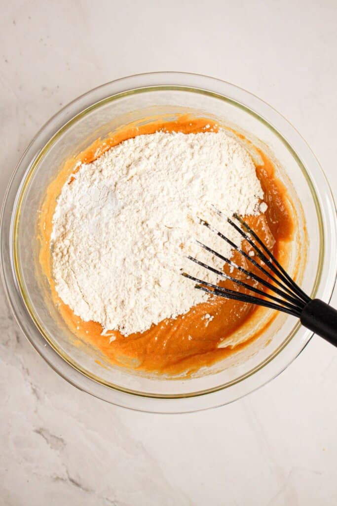 Dry ingredients being added to batter in a glass bowl.