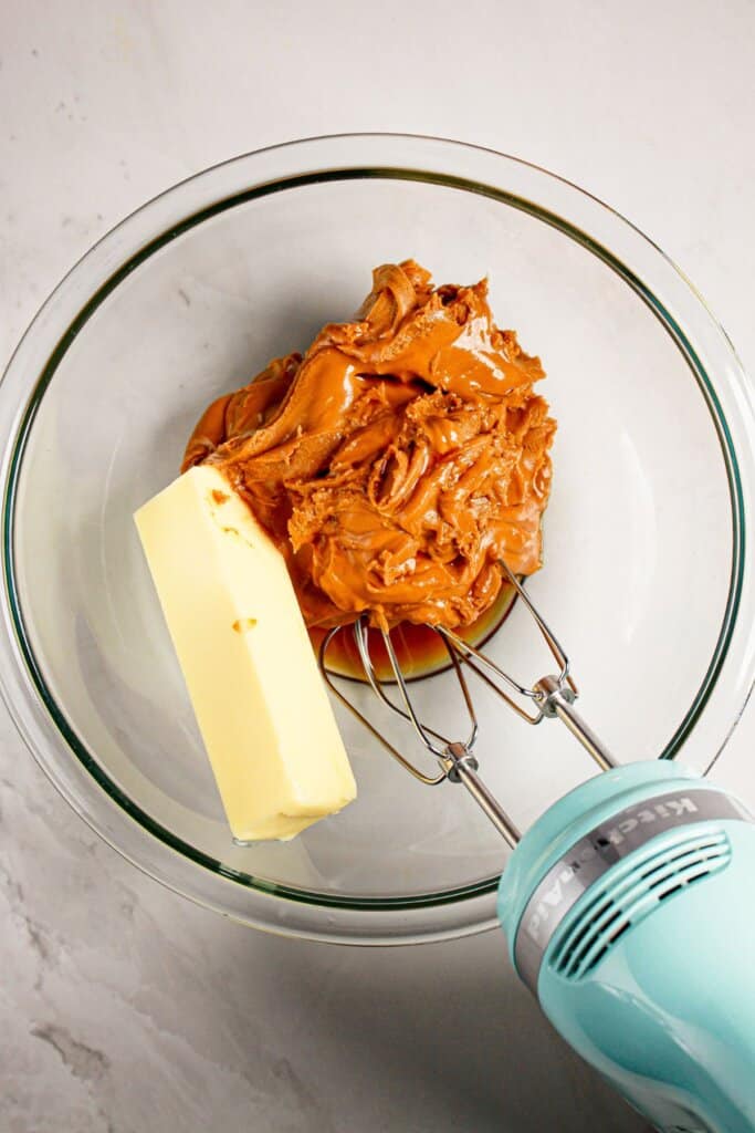 Peanut butter, vanilla, and butter being mixed in a glass mixing bowl.