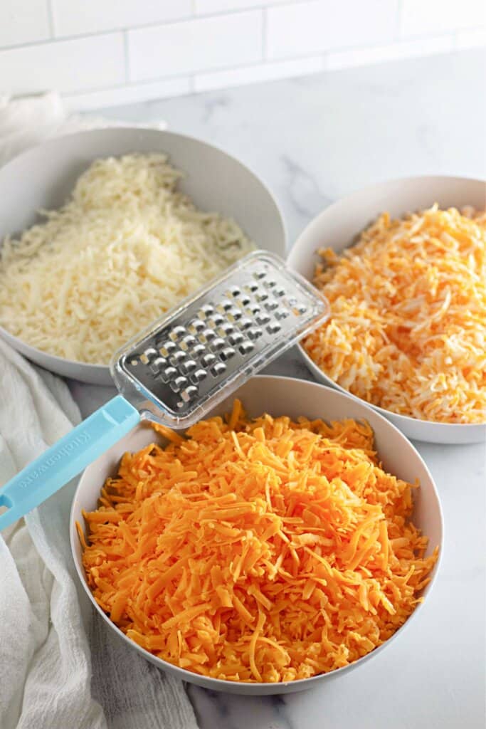 Three bowls of different shredded cheeses.