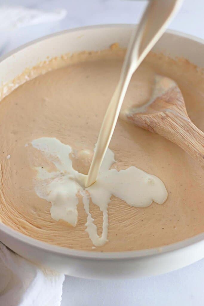 Cream being stirred into a roux in a skillet.