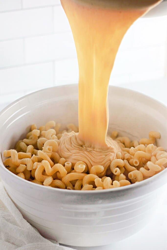Sauce being poured on top of pasta in a mixing bowl,